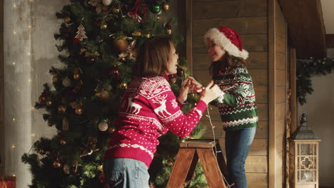Glückliche-Mutter-Und-Tochter-Tanzen-Und-Spielen-Zusammen-Mit-Lichtern,-Während-Sie-Zu-Hause-Den-Weihnachtsbaum-Schmücken-1