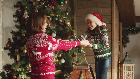 Happy-Mom-And-Daughter-Dancing-And-Playing-Together-With-Lights-While-Decorating-Christmas-Tree-At-Home-2
