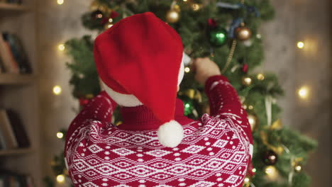 Rückansicht-Des-Mannes,-Der-Eine-Weihnachtsmütze-Aufsetzt-Und-Den-Weihnachtsbaum-Zu-Hause-Schmückt