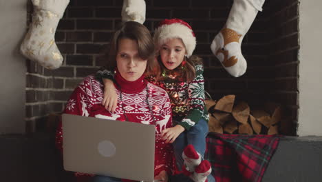 Glückliche-Mutter-Und-Tochter-In-Weihnachtspullovern-Und-Mit-Lichtern-Um-Den-Hals-Sitzen-Auf-Dem-Sofa,-Während-Sie-Den-Laptop-Benutzen-1