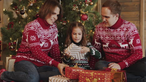 Glückliches-Kleines-Mädchen,-Das-Geschenk-Auspackt,-Während-Sie-Mit-Ihrer-Mutter-Und-Ihrem-Vater-Vor-Dem-Weihnachtsbaum-Zu-Hause-Sitzt