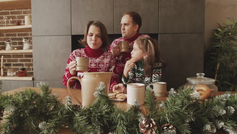 Familia-Feliz-En-Suéteres-Navideños-Bebiendo-Y-Comiendo-Galletas-El-Día-De-Navidad-En-Casa