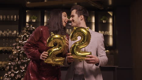 Frau-Und-Mann-In-Eleganter-Kleidung,-Die-Luftballons-Mit-Den-Zahlen-22-Halten,-Während-Sie-Auf-Der-Neujahrsparty-Tanzen