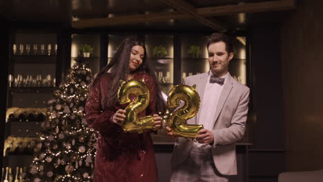 Frau-Und-Mann-In-Eleganter-Kleidung,-Die-Luftballons-Mit-Den-Nummern-22-Halten,-Während-Sie-Auf-Der-Neujahrsparty-1-Tanzen
