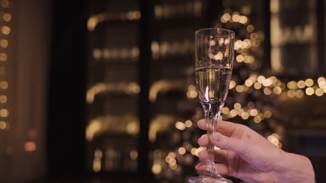 Camera-Focuses-On-The-Hand-Of-A-Woman-Holding-A-Glass-Of-Champagne-At-The-New-Year's-Party