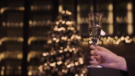 Camera-Focuses-On-The-Hand-Of-A-Woman-Holding-A-Glass-Of-Champagne-At-The-New-Year's-Party-1