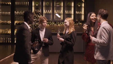 Group-Of-Friends-Wearing-Elegant-Clothes-Talking-While-They-Holding-Champagne-Glasses-In-New-Year's-Party