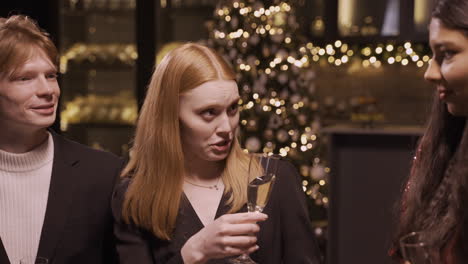 Close-Up-View-Of-A-Red-Haired-Girl-Wearing-Elegant-Clothes-While-Talking-With-Her-Friends-And-Holding-A-Glass-Of-Champagne-At-The-New-Year's-Party-1