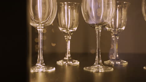 Close-Up-View-Of-Several-Empty-Crystal-Glasses-On-Wooden-Table,-Reflected-Christmas-Lights