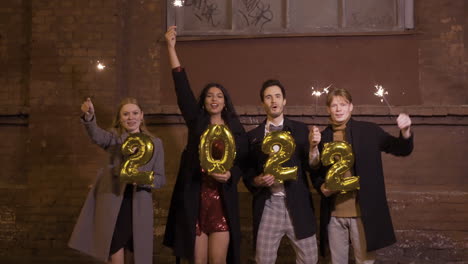 Gruppe-Von-Freunden-In-Eleganter-Kleidung-Mit-Wunderkerzen-Und-2022-Nummerierten-Goldenen-Luftballons-Auf-Der-Straße-Nach-Der-Neujahrsparty-1