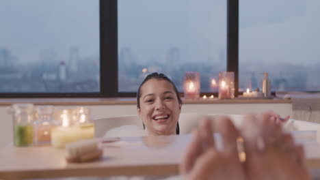 Close-Up-View-Of-Woman-Feet,-She-Looking-And-Smiling-At-Camera-While-Taking-A-Bath-In-The-Bathtub-Decorated-By-A-Wooden-Table-With-Candles
