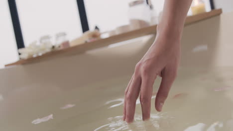 Nahaufnahme-Der-Hände-Einer-Frau,-Die-Das-Wasser-Einer-Badewanne-Mit-Blumen-Berühren-1