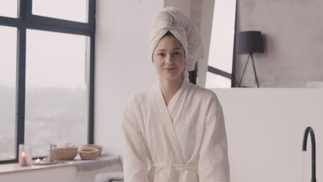 Front-View-Of-A-Woman-Sitting-Posing-And-Smiling-At-The-Camera-With-A-Towel-On-Her-Head-And-A-Bathrobe