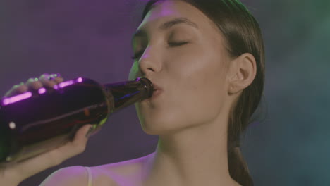 Close-Up-Of-A-Beautiful-Girl-With-Closed-Eyes-Drinking-Beer-And-Dancing-At-Disco