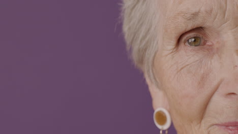 Close-Up-View-Of-Senior-Woman-Half-Face-With-Short-Hair-And-Green-Eyes-Wearing-Earrings-Posing-With-Serious-Expressiont-Camera-On-Purple-Background