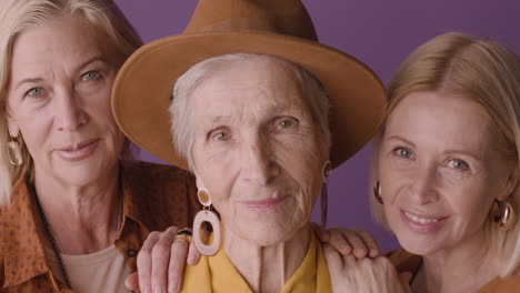 Nahaufnahme-Einer-älteren-Frau-Mit-Hut-Und-Senfhemd-Posiert-Mit-Zwei-Blonden-Reifen-Frauen-Auf-Violettem-Hintergrund