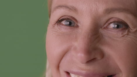Close-Up-View-Of-Half-Face-Of-Blonde-Mature-Woman-With-Blue-Eyes-Smiling-At-Camera-On-Green-Background