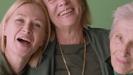 Close-Up-View-Of-Two-Blonde-Mature-Women-And-Blonde-Senior-Woman-Smiling-And-Hugging,-Wearing-Green-Tones-Clothes-And-Posing-On-Green-Background