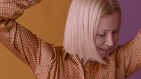 Nahaufnahme-Einer-Glücklichen-Blonden-Reifen-Frau-Mit-Braunem-Hemd,-Die-Auf-Orangefarbenem-Und-Violettem-Hintergrund-Tanzt-Und-Lächelt