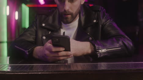 Close-Up-Of-A-Bearded-Man-Using-Mobile-Phone-And-Drinking-While-Sitting-At-Bar-Counter