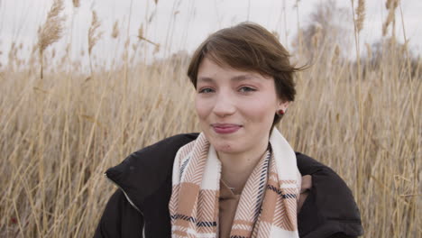 Close-Up-View-Of-A-Teenage-Girl-With-Short-Hair-And-Winter-Clothes-Looking-At-Camera-And-Touching-Her-Hair-In-A-Wheat-Field