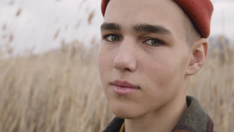 Close-Up-View-Of-A-Teenage-Boy-With-Orange-Beanie-And-Plaid-Coat-Looking-At-Side-In-A-Wheat-Field,-Then-Looks-At-Camera-And-Smiles-1