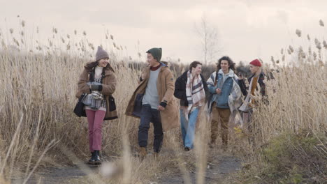 Front-View-Of-A-Group-Of-Teenage-Boys-And-Girls-Wearing-Winter-Clothes-Walking-In-A-Wheat-Field-On-A-Cloudy-Day