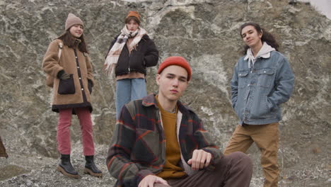 Close-Up-View-Of-Group-Of-Teenage-Friends-Dressed-In-Winter-Clothes-Posing-Looking-At-Camera,-Sitting-And-Standing-On-The-Mountain