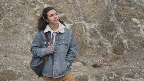 Front-View-Of-A-Teenage-Boy-With-Long-Hair-And-Winter-Clothes-On-The-Mountain-On-A-Windy-Day