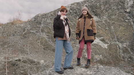 Front-View-Of-Two-Teenage-Girls-In-Winter-Clothes-Posing-At-Camera-On-The-Mountain-On-A-Windy-Day