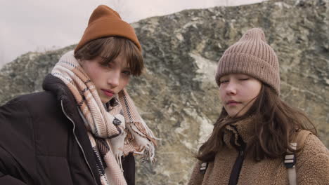 Close-Up-View-Of-Two-Teenage-Girls-In-Winter-Clothes-Posing-At-Camera-On-The-Mountain-On-A-Windy-Day