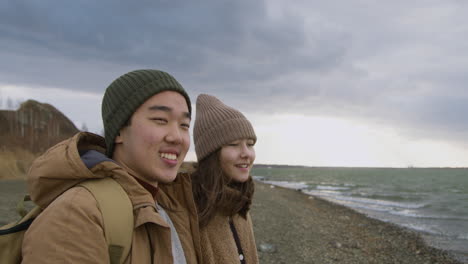 Nahaufnahme-Von-Zwei-Teenagern-In-Winterkleidung-An-Der-Küste,-Die-An-Einem-Windigen-Tag-Sprechen-Und-Auf-Den-Ozean-Schauen
