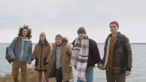 Eine-Gruppe-Teenager-Freunde-In-Winterkleidung-Hält-An-Einem-Windigen-Tag-Die-Hände-Und-Hebt-Die-Arme-Auf-Dem-Berg-Am-Strand