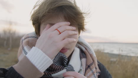 Close-Up-View-Of-Teenage-Girl-With-Short-Hair-And-Winter-Clothes-Looking-At-Camera-And-Smiling-On-Seashore-On-Windy-Day
