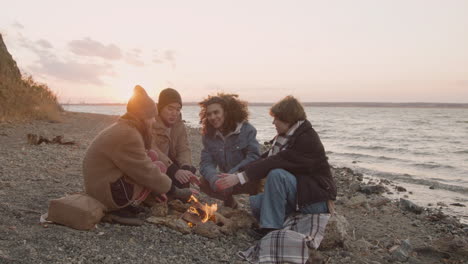 Group-Of-Teenage-Friends-Talking-And-Warming-Their-Hands-At-The-Bonfire-Next-To-The-Seashore
