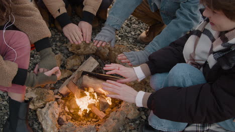 Die-Kamera-Fokussiert-Die-Hände-Einer-Gruppe-Von-Teenagern-In-Der-Nähe-Des-Lagerfeuers