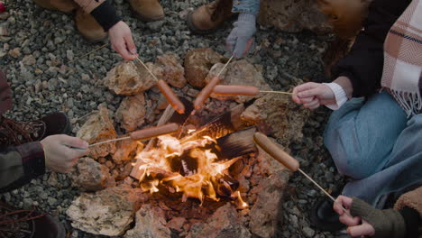 Top-View-Of-Hands-Of-A-Group-Of-Teenage-Friends-Roasting-Sausages-On-The-Bonfire