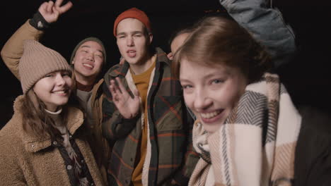 Close-Up-View-Of-Group-Of-Friends-Dressed-In-Winter-Clothes-Waving-At-The-Camera-At-Night