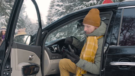 Man-Dressed-In-Winter-Clothes-Searching-In-Smartphone-Sitting-In-The-Car-With-The-Door-Open-In-A-Snowy-Forest