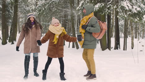 Front-View-Of-Parents-And-Daughter-Dressed-In-Winter-Clothes-Walking-And-Jumping-In-Snowy-Forest