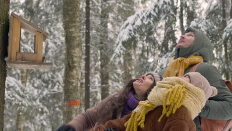 Close-Up-View-Of-Father,-Mother-And-Daughter-Dressed-In-Winter-Clothes-Are-In-Front-Of-A-Tree-Looking-Up-In-A-Snowy-Forest