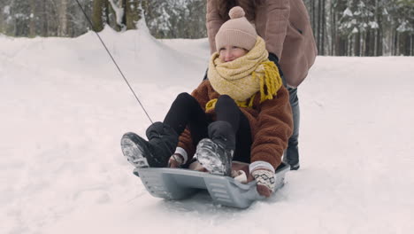 Father-And-Mother-Help-Their-Daughter-To-Ride-On-Sled-In-Snowy-Forest