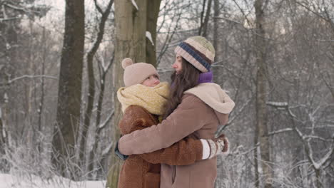 Front-View-Of-Mother-And-Daughter-In-Winter-Clothes-Hugging-In-A-Snowy-Forest