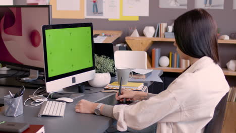 Female-Graphic-Designer-Using-Digital-Drawing-Tablet-And-Looking-At-Monitor-With-Green-Screen-In-An-Animation-Studio-1