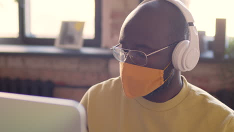 Portrait-Of-An-Man-With-Headphones-And-Face-Mask-Working-On-Computer-In-An-Animation-Studio