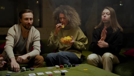 Eine-Gruppe-Von-Freunden,-Die-Poker-Spielen,-Sitzen-Auf-Der-Couch,-Während-Sie-Kartoffelchips-In-Einer-Großen-Glasschüssel-Essen