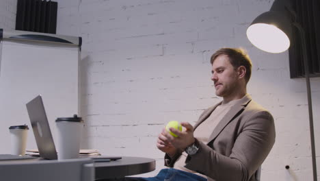 Geschäftsmann,-Der-Auf-Laptop-computer-Tippt-Und-Dann-Mit-Tennisball-Spielt,-Während-Er-Am-Tisch-Im-Sitzungssaal-Sitzt