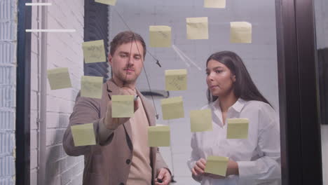 Businessman-And-Businesswoman-Brainstorming-With-Sticky-Notes-On-Glass-Window-2