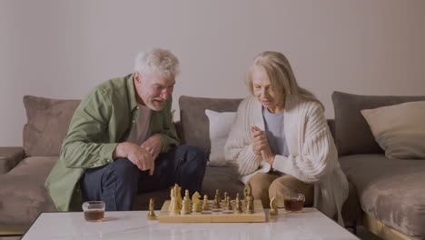 Senior-Mann-Und-Frau-Spielen-Schach,-Während-Sie-Zu-Hause-Auf-Dem-Sofa-Sitzen