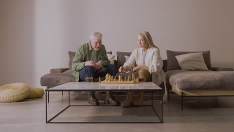 älterer-Mann-Und-Frau-Spielen-Schach,-Während-Sie-Zu-Hause-Auf-Dem-Sofa-Sitzen-1
